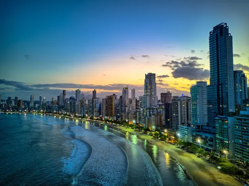 Vista do pôr do sol da praia de Balneário Camboriú, com prédios ao redor da orla.